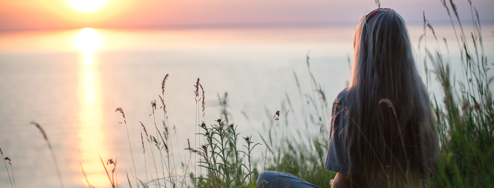 woman sitting at the water at sunset meditating